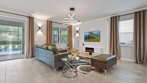 A modern living room with a sofa, ottoman, glass coffee table, and a fireplace. - Star Wars & Encanto Bunk Rooms + Pool @ Storeylake (Kissimmee)