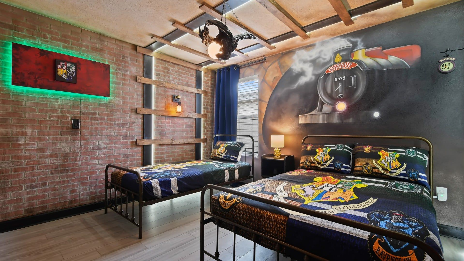 A room with a brick wall, a ceiling with exposed beams, a bed with a Hogwarts Express themed duvet, and a wall mural of a Hogwarts Express train.