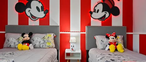 Una habitación con dos camas, cada una con cabecero de Mickey Mouse. Entre las camas hay una mesita de noche con una lámpara y una figurita de Mickey Mouse.