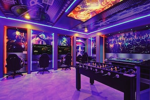 A gaming room with multiple gaming stations, a foosball table, and vibrant wall art. - Lakeview 10br Pool, Spa & Star Wars Game Room (Kissimmee)
