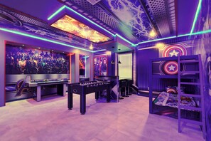 A room with a foosball table, a bed with a Captain America themed headboard, and a wall with a large Avengers movie poster. - Lakeview 10br Pool, Spa & Star Wars Game Room (Kissimmee)