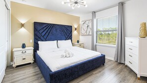 A bedroom with a large bed, bedside tables, a nightstand, a window with blinds, and a decorative vase. - 8BR Family Getaway Private Pool (Kissimmee)