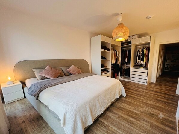 A bedroom with a bed, bedside table, wardrobe, and a hanging light fixture.