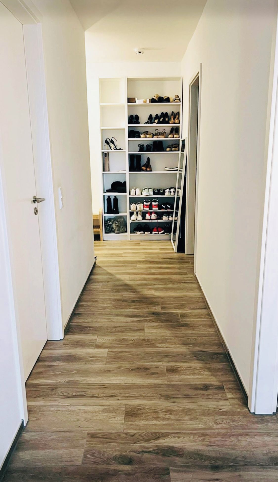 Ein Flur mit Holzboden, der zu einem Schuhregal mit mehreren Ablagen führt.