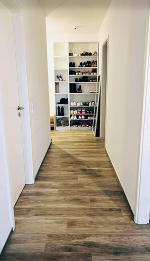 A hallway with a wooden floor leading to a shoe storage area with multiple shelves.