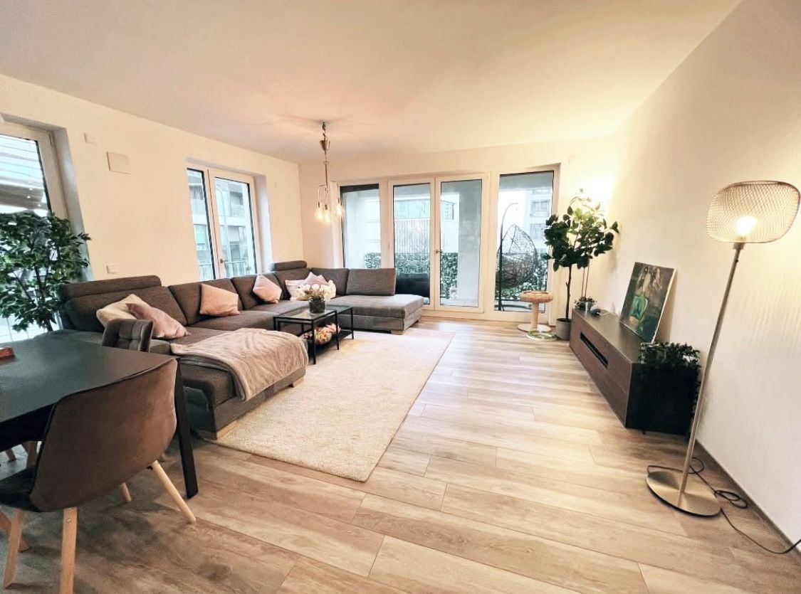Ein modernes Wohnzimmer mit einer Sofagarnitur, einem Esstisch und einer Stehlampe.