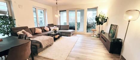 Ein modernes Wohnzimmer mit einer Sofagarnitur, einem Esstisch und einer Stehlampe.
