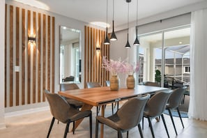 A modern dining area with a wooden table and chairs, pendant lights, and a vase with flowers. - Family Retreat w/ Circus Lounge & Game Room (Davenport)