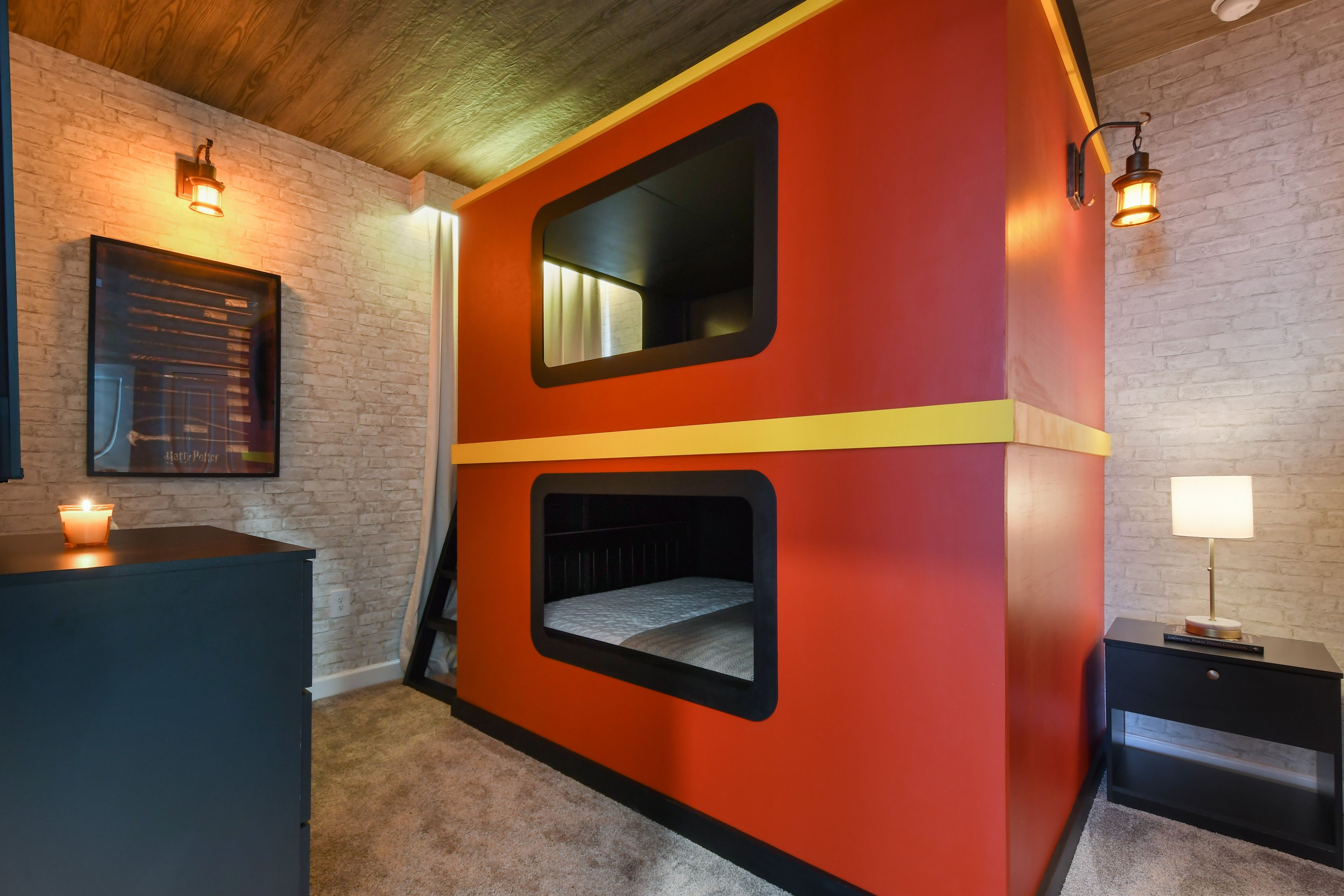 Una habitación con una pared roja y amarilla, un cuadro enmarcado, una mesita con una vela y una lámpara.