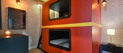 Una habitación con una pared roja y amarilla, un cuadro enmarcado, una mesita con una vela y una lámpara.