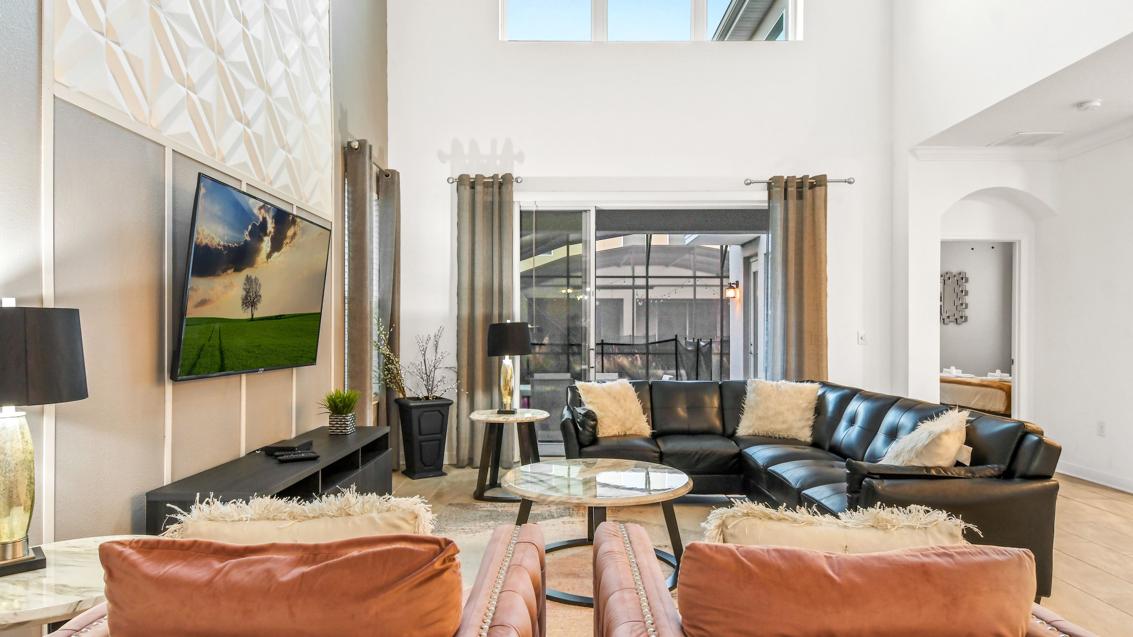 A modern living room with a black leather sofa, a glass coffee table, and a flat-screen TV mounted on the wall.