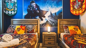 A bedroom with two beds, each with Gryffindor and Slytherin themed bedding, a poster of a wizard on the wall, and a nightstand with a lamp. - Harry Potter, Mickey & Space Rooms + Theater! (Davenport)