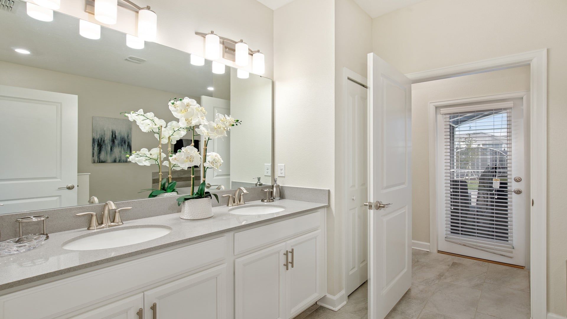 A bathroom with a double sink vanity, a large mirror, and a door leading to a balcony.
