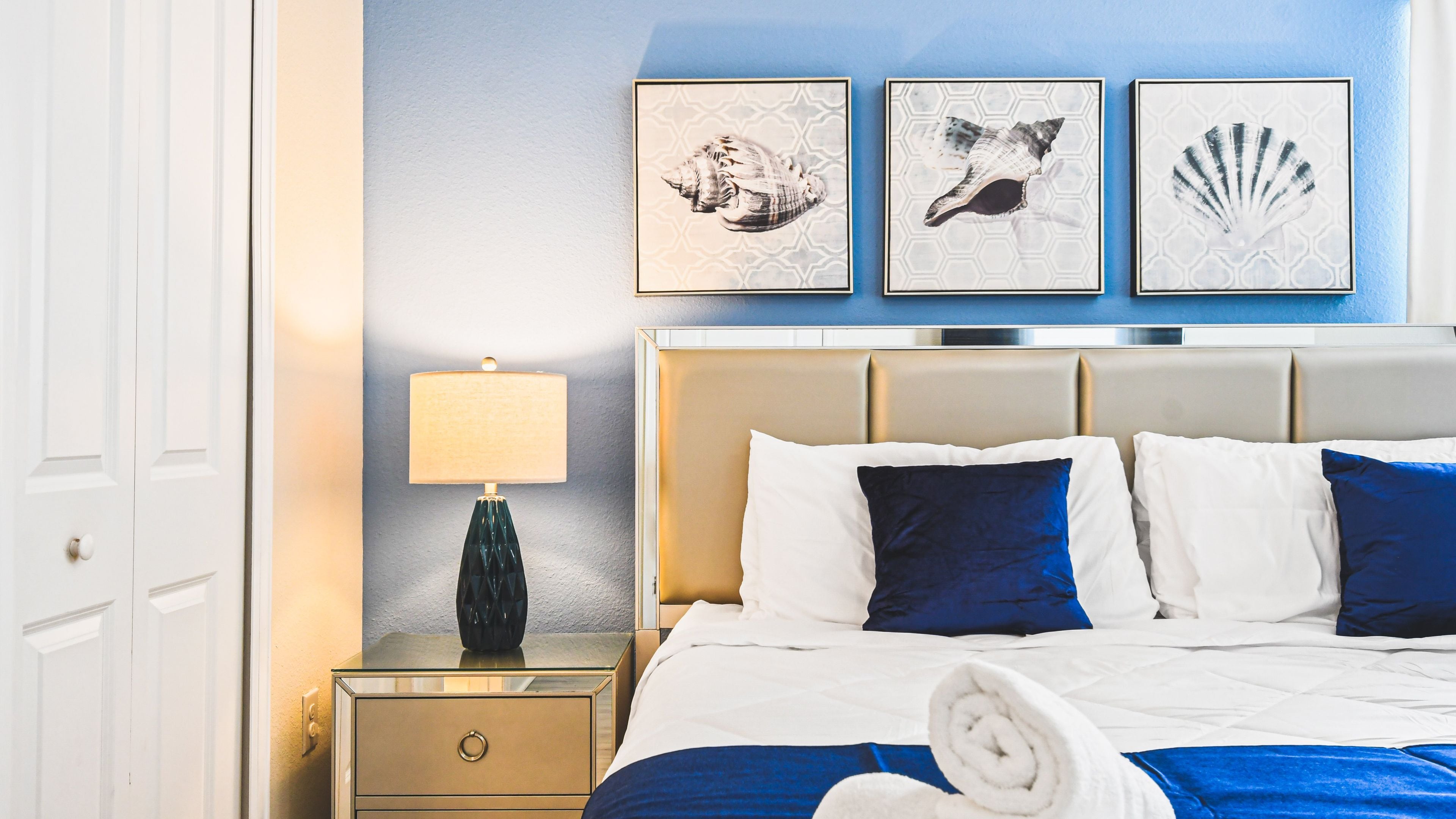 A hotel room with a bed, a nightstand, a lamp, and three framed pictures on the wall.