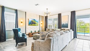 A spacious living room with a large sectional sofa, a comfortable armchair, and a dining area. There is a large window with a view of a swimming pool and greenery outside. - Harry Potter, Mickey & Space Rooms + Theater! (Davenport)