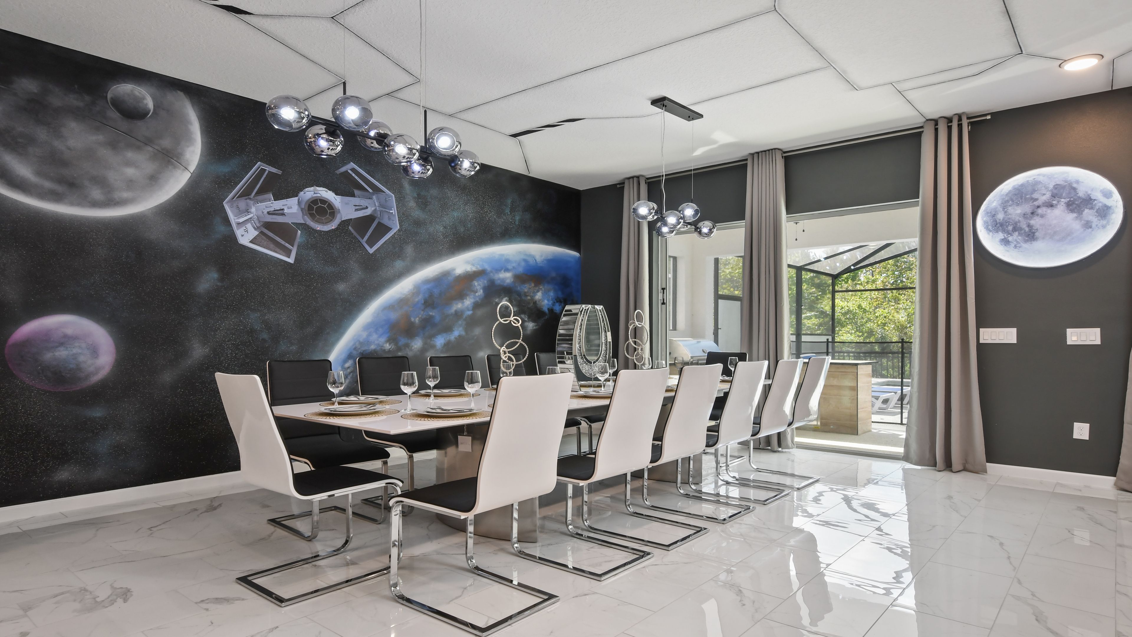 A dining area with a space-themed mural, a modern chandelier, and a view to the outdoors.