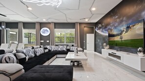 A modern living room with a sectional sofa, a flat-screen TV, and a large window. - Minions, Star Wars, & Frozen-themed Family Retreat (Kissimmee)