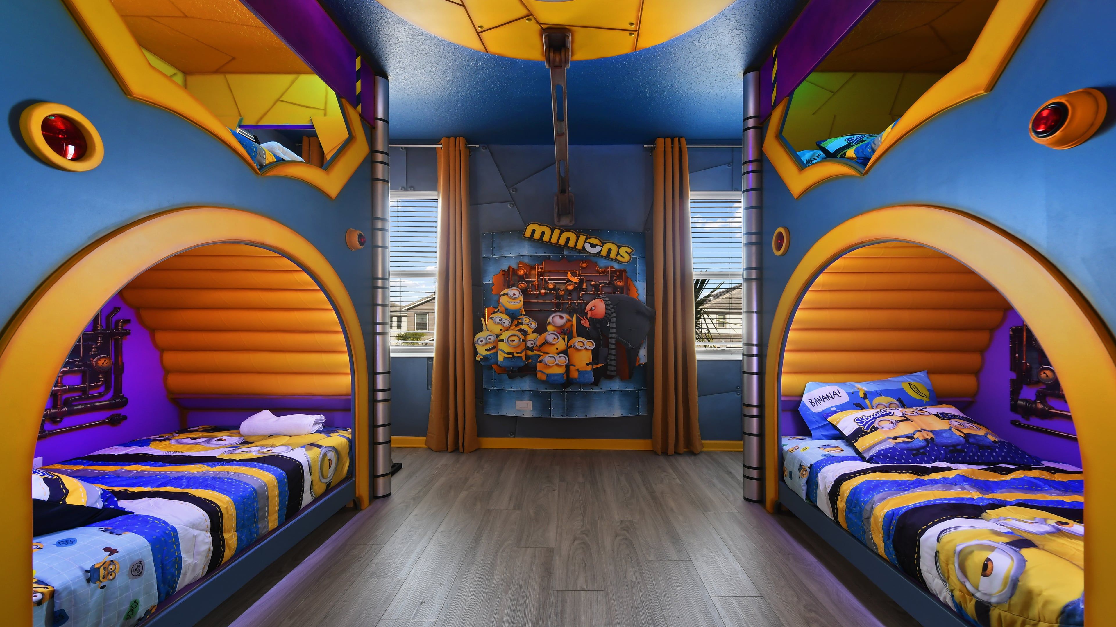 A room with two beds, a Minions-themed poster, and a window with blinds.