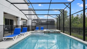 A swimming pool with blue lounge chairs and a hot tub, surrounded by a glass enclosure and a black fence. - Minions, Star Wars, & Frozen-themed Family Retreat (Kissimmee)