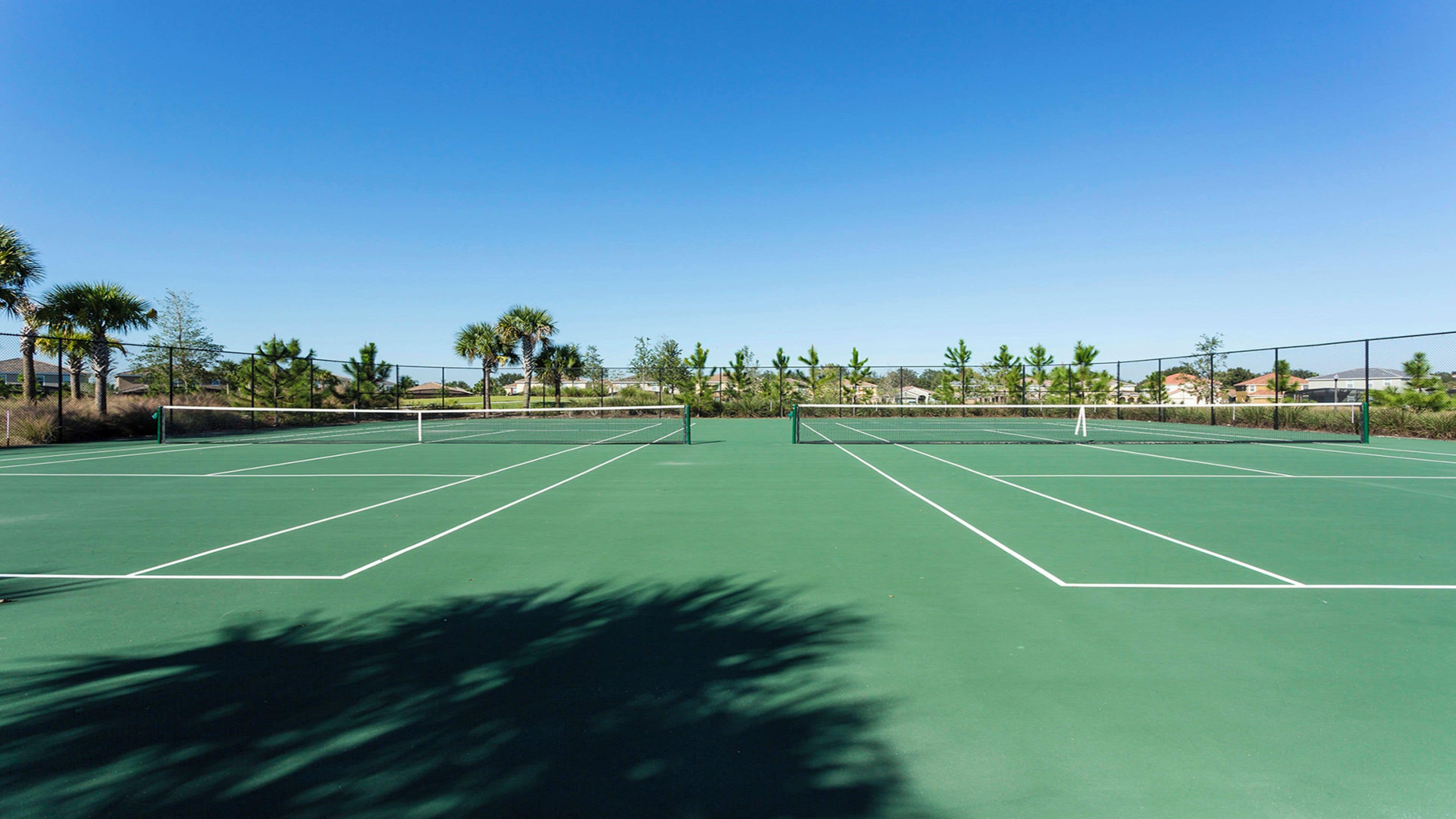 A tennis court with a net, surrounded by trees and houses.