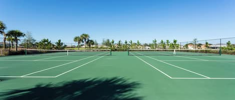 Una cancha de tenis con red, rodeada de árboles y casas.