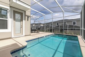 Ein Swimmingpool mit klarem, blauem Wasser, umgeben von einer überdachten Terrasse mit Tisch und Stühlen.