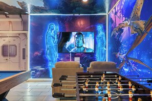 A room with a foosball table, a television, and a mural of a fantasy scene. - Avatar Game Room + Harry Potter BR w/ Pool~spa (Kissimmee)