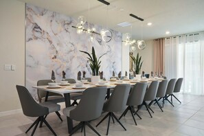 Une salle à manger moderne avec un mur en marbre, une longue table dressée pour un repas et des chaises contemporaines.