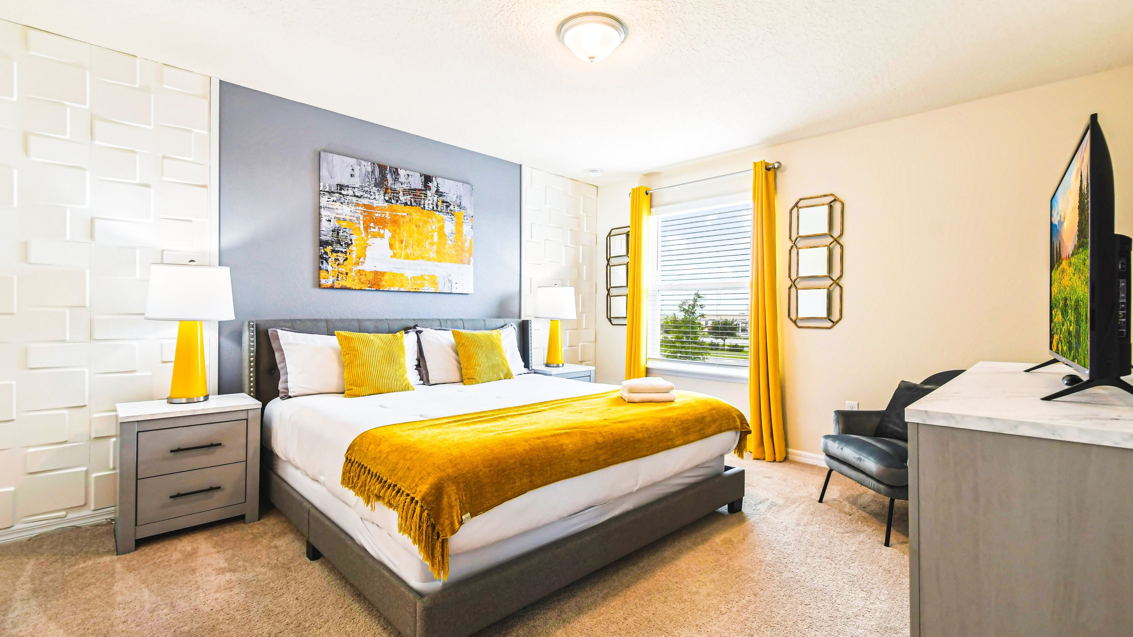 A modern hotel room with a large bed, two bedside tables, a desk, a chair, a TV, and a window with curtains.