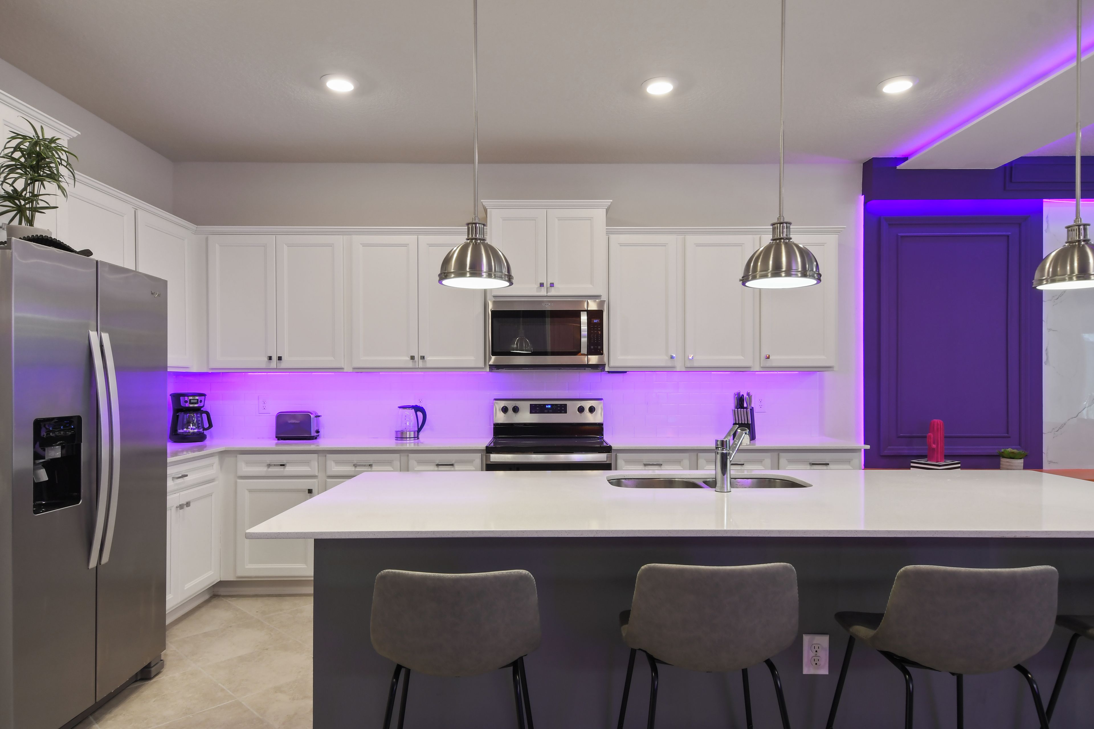 A modern kitchen with white cabinets, stainless steel appliances, a central island with bar stools, and pendant lighting.