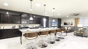 A modern kitchen with dark cabinets, a central island with bar stools, and a dining area with a sofa and coffee table. - Star Wars/harrypotter Bunks, Pool, Lake View, 8br! (Kissimmee)