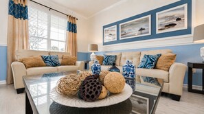 A living room with two sofas, a coffee table with decorative items, and a wall with framed artwork. - 6BR Windsor Hills Pool & Themed Rooms (Kissimmee)