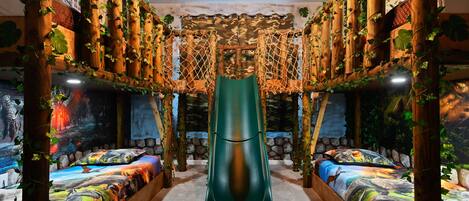 A room with a green slide, two beds with colorful bedding, and walls covered in greenery and murals.