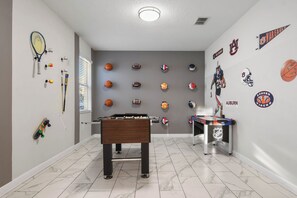 A room with a foosball table, a basketball hoop, and various sports memorabilia on the walls. - Green View Villa: 6 Beds, Pool & Resort Access (Davenport)