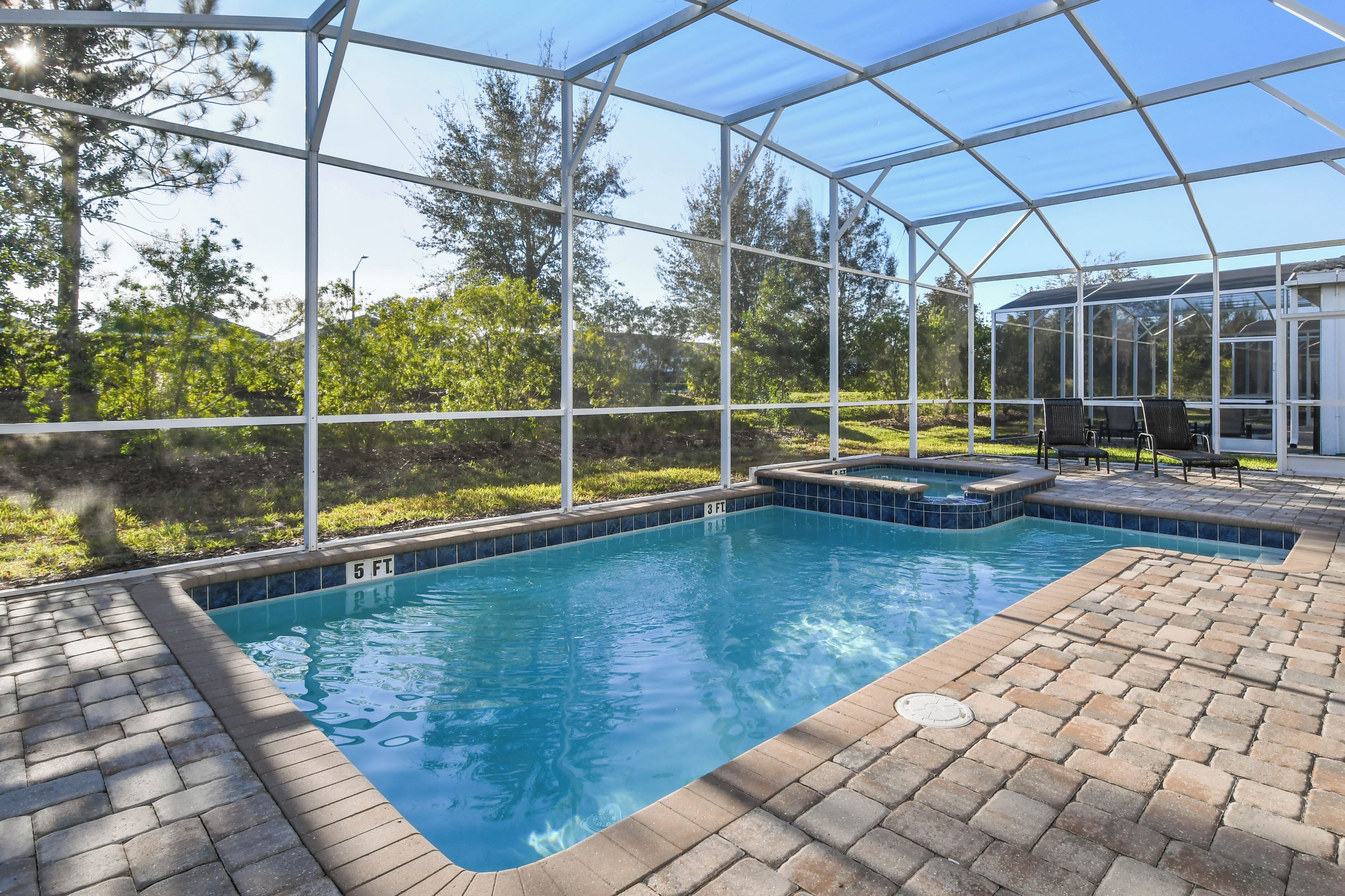 A swimming pool with a glass enclosure, surrounded by brick flooring, and a hot tub area.