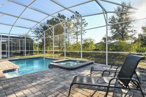 A covered outdoor swimming pool with a hot tub, surrounded by a brick patio and metal chairs. - Green View Villa: 6 Beds, Pool & Resort Access (Davenport)