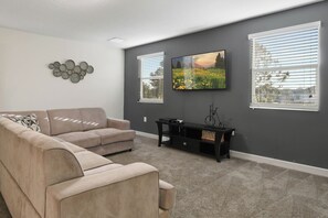 A living room with a beige sofa, a flat-screen TV mounted on the wall, and a black entertainment unit. - Green View Villa: 6 Beds, Pool & Resort Access (Davenport)