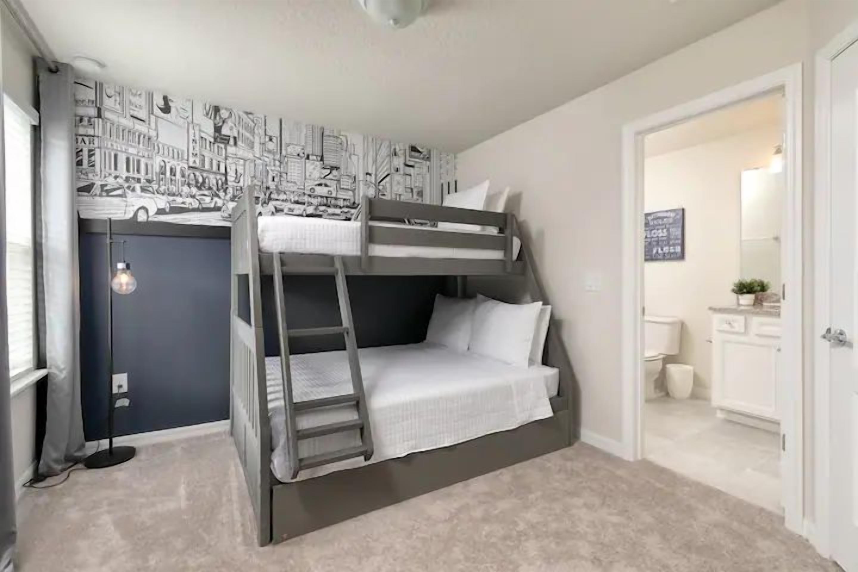 A bunk bed with a ladder, a desk, and a chair in a room with a cityscape wall mural.