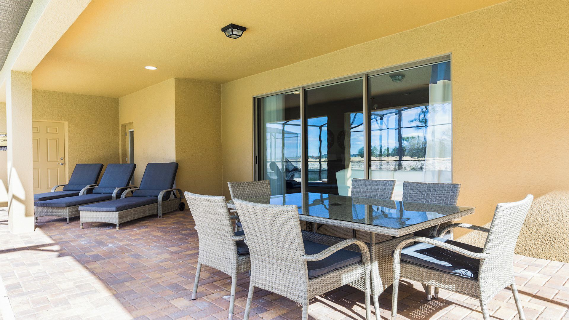 Un patio soleado con una mesa de vidrio y sillas de mimbre, con vistas a un paisaje pintoresco.