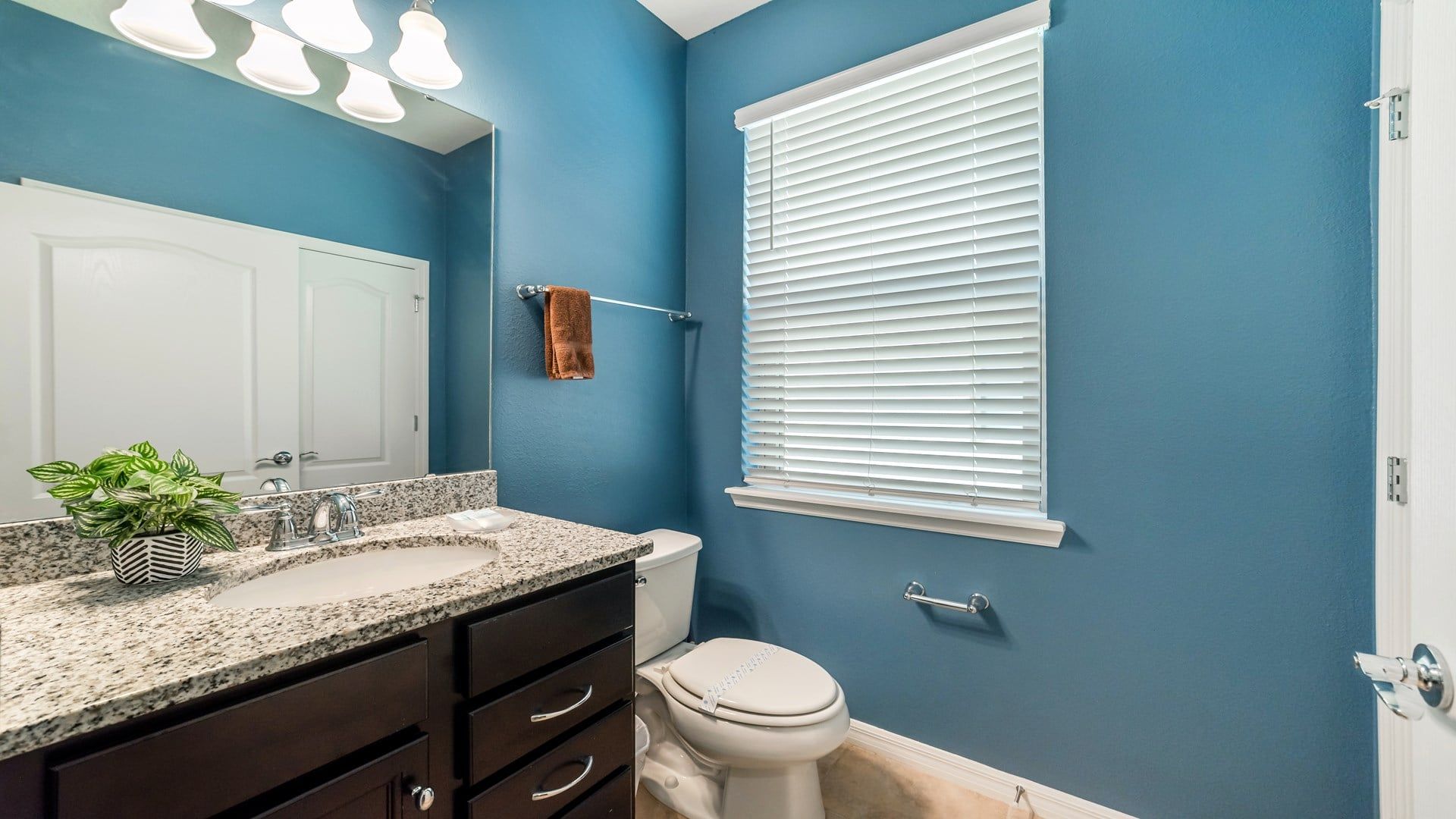 A bathroom with a blue wall, a white toilet, a sink with a granite countertop, and a mirror above the sink.