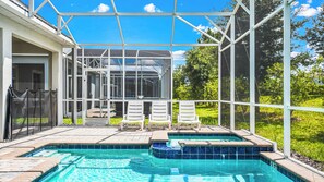 A swimming pool with a glass enclosure, three white lounge chairs, and a view of a house. - Luxe Villa With Stunning Pool & Resort Access (Davenport)
