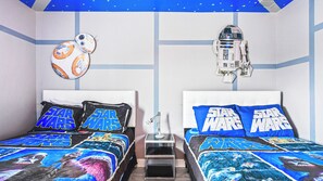 Un dormitorio con ropa de cama temática de Star Wars, dos camas, una mesita de noche y un techo con diseño de estrellas.