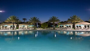 A swimming pool with lounge chairs and umbrellas, surrounded by palm trees and buildings with tiled roofs. - Luxe Villa With Stunning Pool & Resort Access (Davenport)