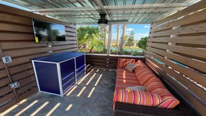 A covered outdoor living area with a sofa, a TV mounted on the wall, and a blue cabinet. - Family Home w Large Dining~frozen Room~resort Pool (Davenport)
