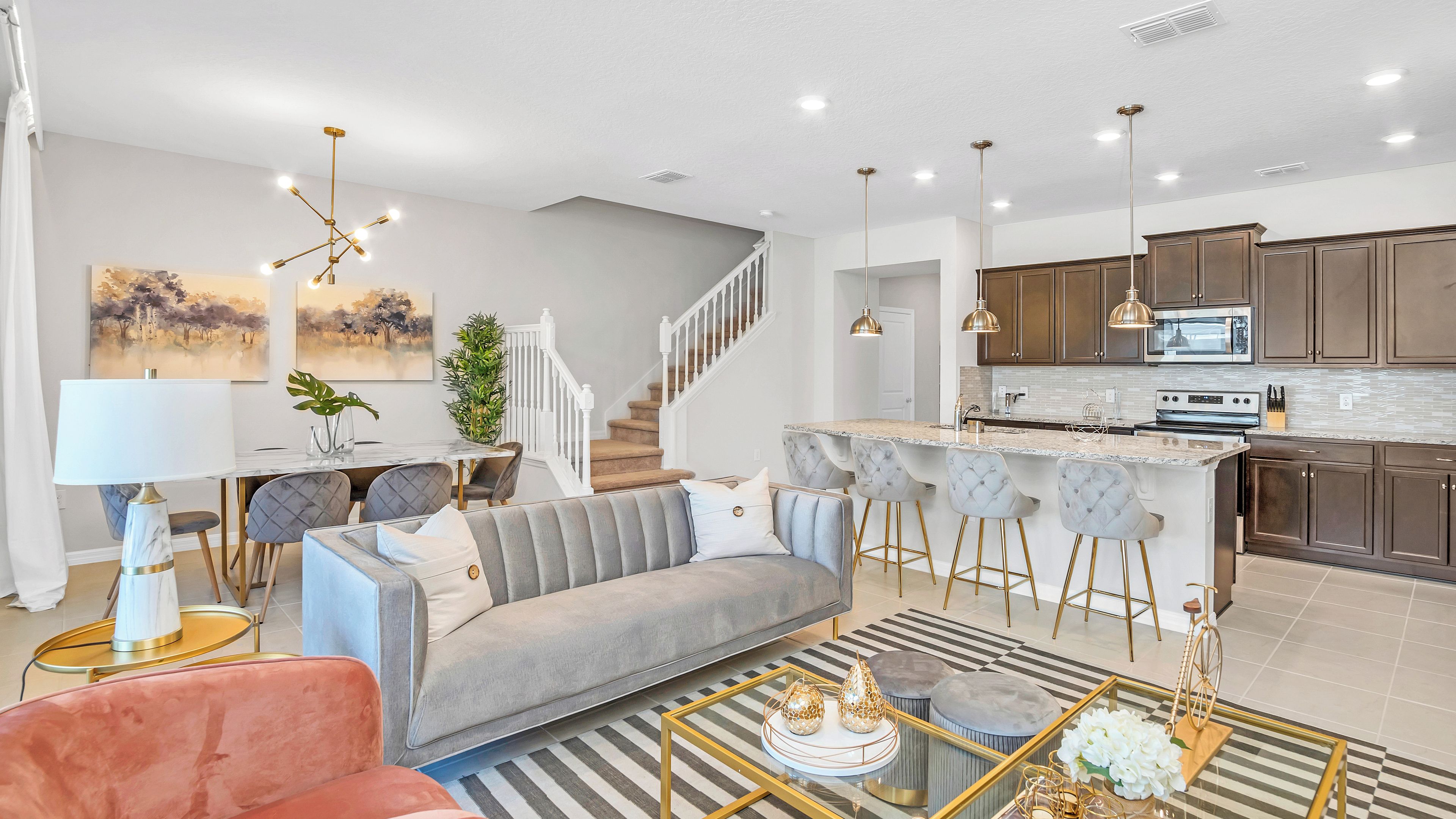 A modern living room with a sofa, a dining area, and a kitchen with dark cabinets and a marble countertop.