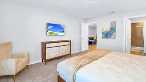 A bedroom with a bed, a dresser, a chair, a TV, and an open door leading to another room. - Family Home w Large Dining~frozen Room~resort Pool (Davenport)