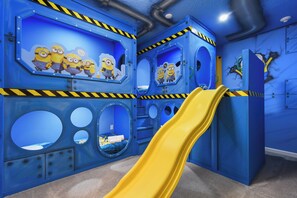 A play area with a yellow slide, circular windows, and Minion-themed decorations. - Luxe Stay! Spider-man Arcade & Theater Near Disney (Kissimmee)