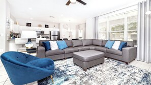 A modern living room with a sectional sofa, a blue armchair, and a large window with blinds. - Close2parks, 7br, Themed Room @ Windsor Hill! (Kissimmee)