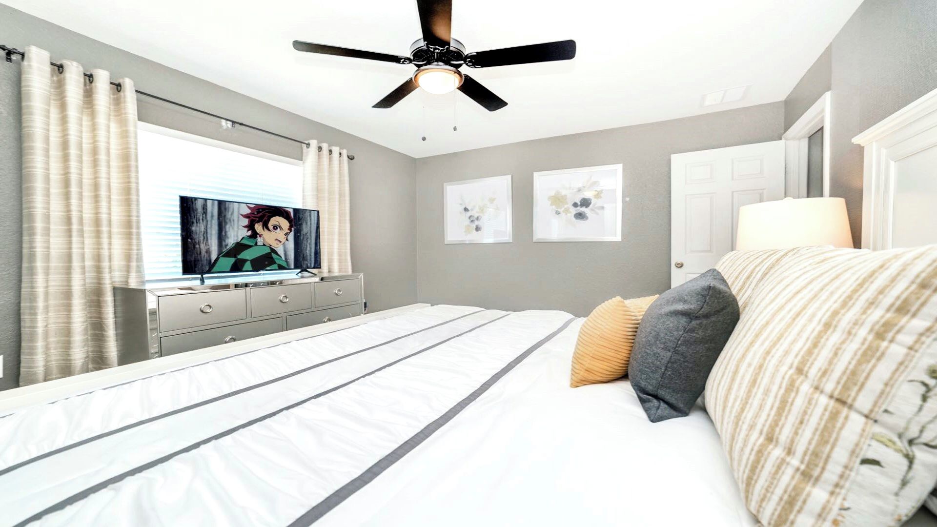 Een slaapkamer met een bed, een plafondventilator, een televisie en kunstwerken aan de wanden.