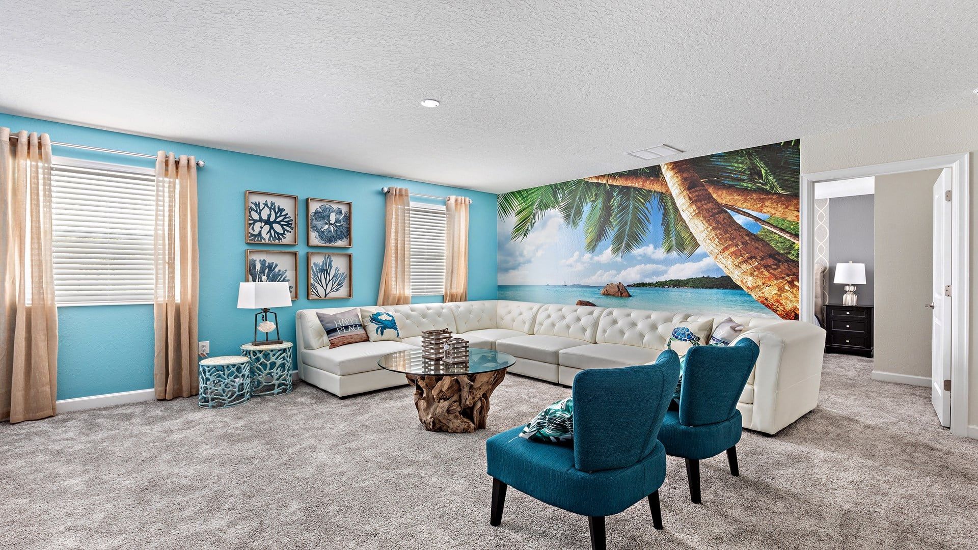 A living room with a large sectional sofa, two blue armchairs, a coffee table, and a wall mural of a beach scene.